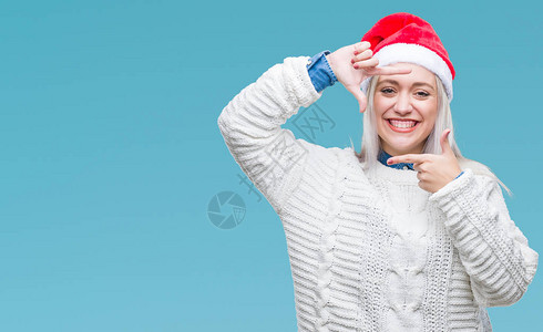 穿着圣诞帽的年轻金发女郎在孤立的中微笑地用手和指搭架图片