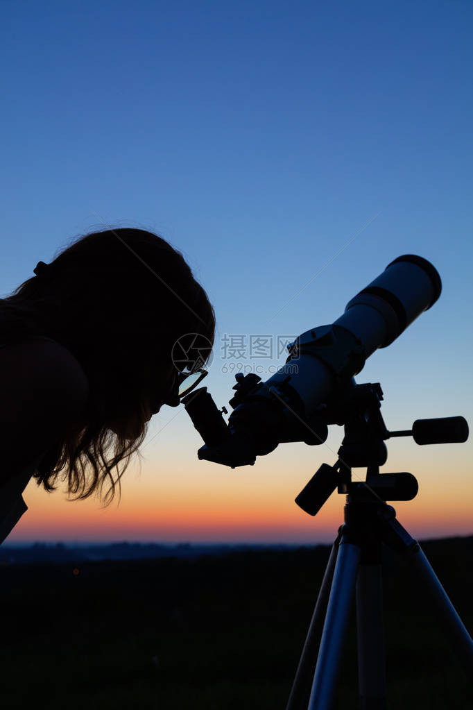 年轻女用天文望远镜看着天空图片