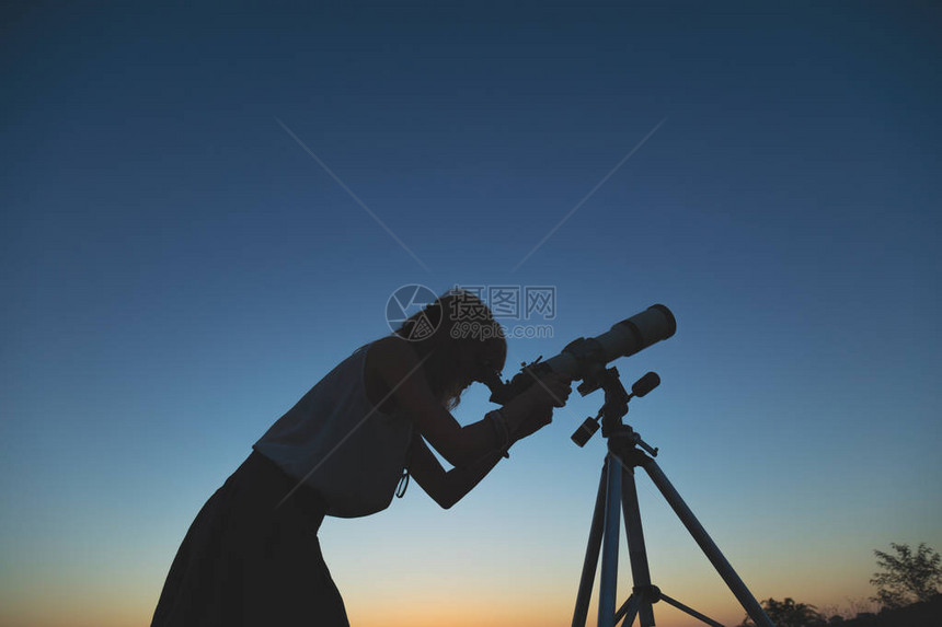 年轻女用天文望远镜看着天空图片