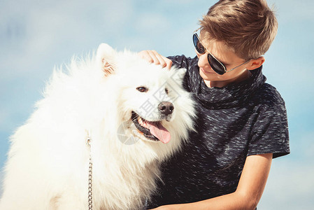 男孩和女孩在海边度假快乐的11岁男孩在海边拥抱他的狗品种萨摩耶图片