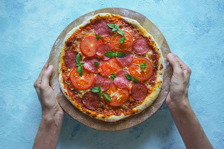 手拿西红柿和香肠的自制披萨图片