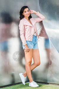 年轻的美国女士身穿浅粉色皮夹克蓝色破洞牛仔短裤白色运动鞋图片