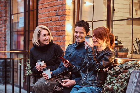 三个快乐的朋友在外边咖啡厅附近坐着喝咖啡休息时图片