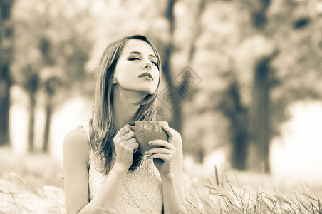 美丽的女孩在公园的草地上坐着一杯咖啡图像以Sepia背景图片
