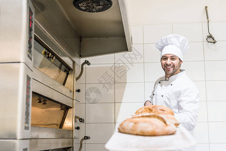 穿着白色厨师帽子的面带微笑的面包师用热新鲜图片