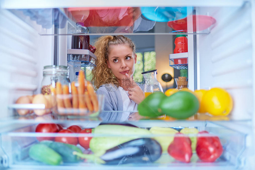 女人站在装满杂货的冰箱前喝果汁从冰箱内图片