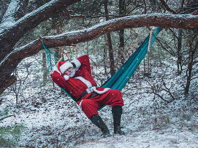 圣诞老人睡在冬季森林的吊床里图片