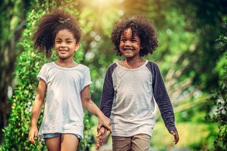 公园里快乐的小男孩和女孩两个非裔美国人的孩子一起在花图片
