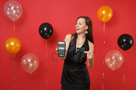 有趣的女孩拿着无线现代银行支付终端处理在鲜红色背景气球上获取信用卡支付黑卡新年快乐模拟背景图片
