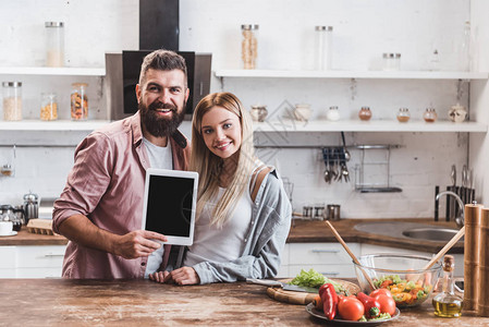 幸福的情侣在木制厨房桌上拿着数字平板背景图片
