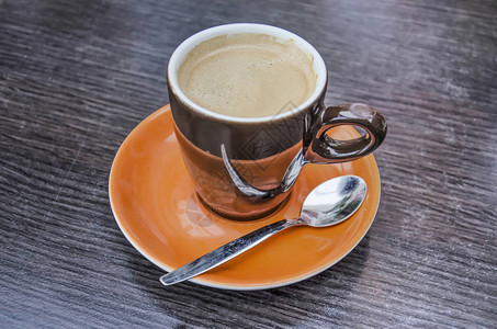 一杯咖啡放在橙色碟子和木桌面上的反图片