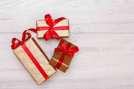 三个带红丝带的礼物盒绑在灰色木质背景上图片