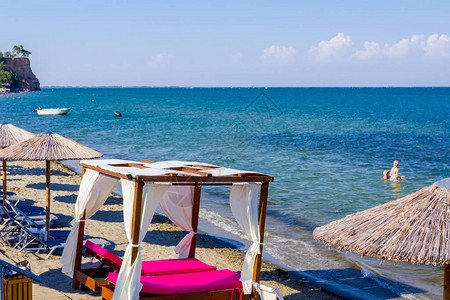 上面的遮阳罩雨伞甲板椅和豪华舒适的木头渡假被放在公共海滩上图片