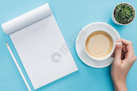 持有咖啡杯空白笔记本和蓝底铅笔的图片
