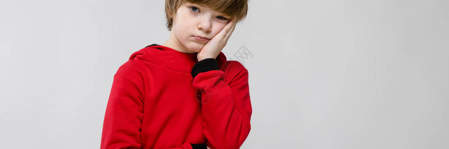 穿着红帽衫的心烦的小男孩脸颊上握着手图片