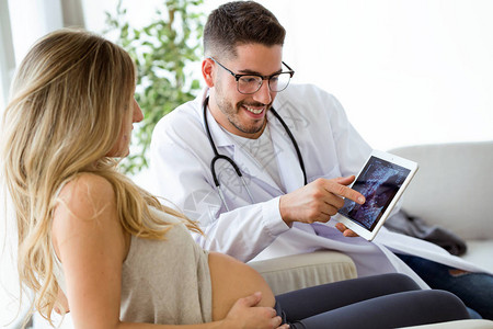 年轻男妇科医生用数码平板电脑向孕妇展示超声波扫描婴图片