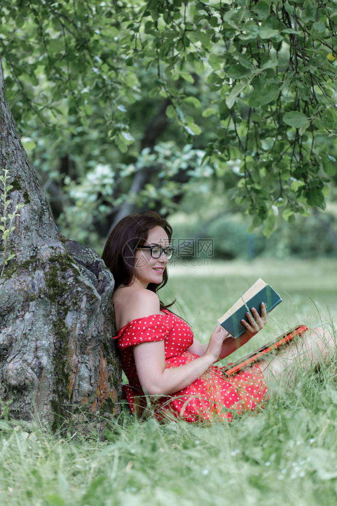 年轻女子坐在树下的草地上看书图片