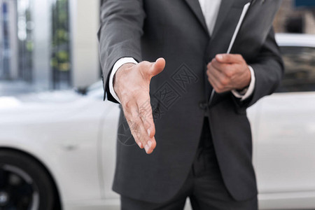男汽车销售员在背景上与汽车握手图片