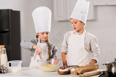 儿童在餐桌边用碗盘煮鸡蛋时戴大厨帽图片