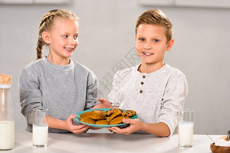 快乐的孩子们拿着盘子和饼干在桌子旁图片
