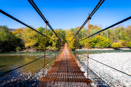 秋天横跨山区河流的狭窄金属脚桥图片