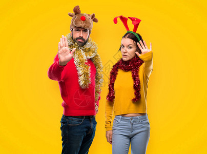 在圣诞节日穿衣服的夫妇手举停止手势否认一种对黄色有错误看法的情况图片