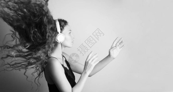 在白色墙前用耳机监听音乐的美丽的年轻美女黑背景图片