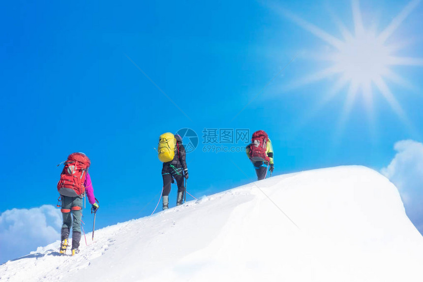 登山者在阳光明媚的冬天到达雪山顶图片