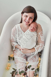 年轻母亲和新生儿在奶水浴中用鲜花洗图片