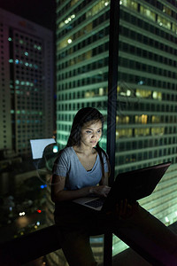 利用笔记本电脑对着玻璃窗在夜间接近城市时拍摄亚洲年轻美图片