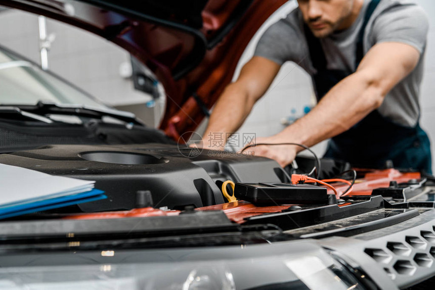 汽车修理工用万表电压表在修理厂检查汽车电池图片