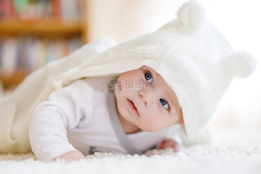 蓝眼睛的女婴在阳光明媚的白色卧室里穿着白色毛巾或冬季工作服新生儿在床上放松儿童托儿所儿童纺织品和床上用品有玩具熊的图片