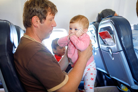 年幼的疲倦父亲和他哭泣的女婴在飞机上度假时图片