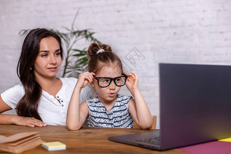 一位带着小女儿的年轻母亲正在使用个人电脑在互联网上购物网上图片