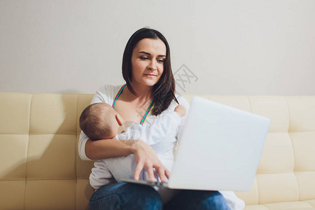 从事笔记本电脑工作的美丽年轻母亲在家为新生儿哺乳妈商业界妇女图片