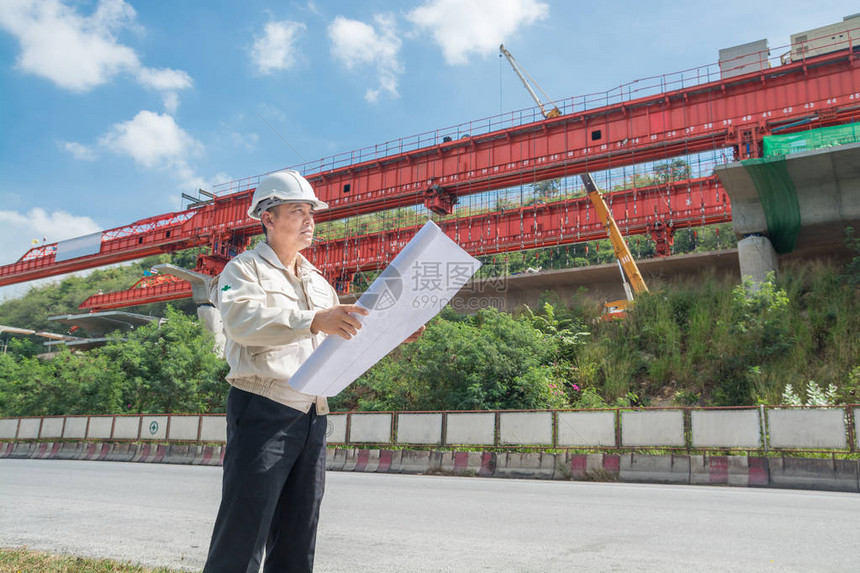 戴着安全帽和安全背心的商人或工程师或建筑师在基础设施工现场旁监督高速公路或公路项目图片