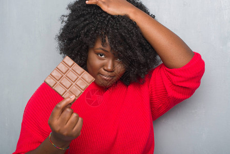 非洲年轻女在灰墙上吃着一根巧克力棒图片