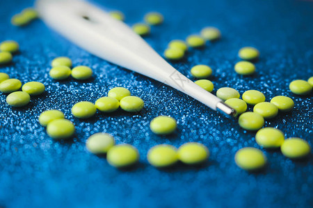 蓝色背景上的小型医用药剂圆形片剂维生素药物和电子数字温度计图片