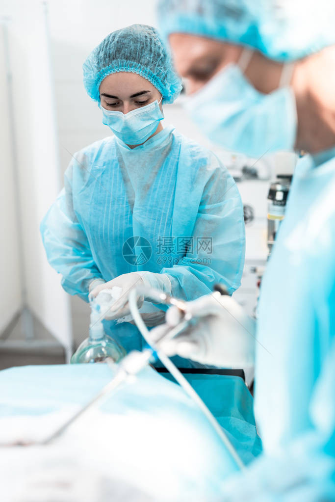 在手术期间向病人提供呼吸支持的戴防护面具和消毒手套的女医务工作者图片
