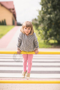 可爱的白人小女孩在斑马路口的黄色街屏障上图片