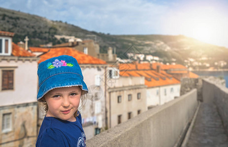 在克罗地亚杜布罗夫尼克老城历史墙上行走的小女孩戴蓝帽图片