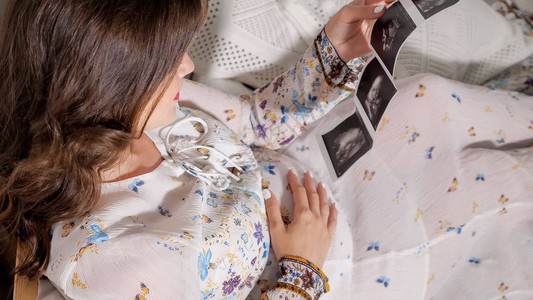 从上面拍摄的孕妇拿着胎儿扫描坐在床上孕妇健康图片