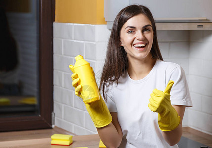 穿着白色T恤戴着黄色橡皮手套的长发快乐女孩在厨房打扫时笑并拿图片