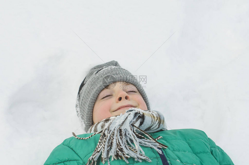 穿着帽子围巾和绿外套的男孩躺在雪地背上图片