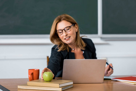 女教师坐在计算机桌上在课堂上伸手求苹果图片