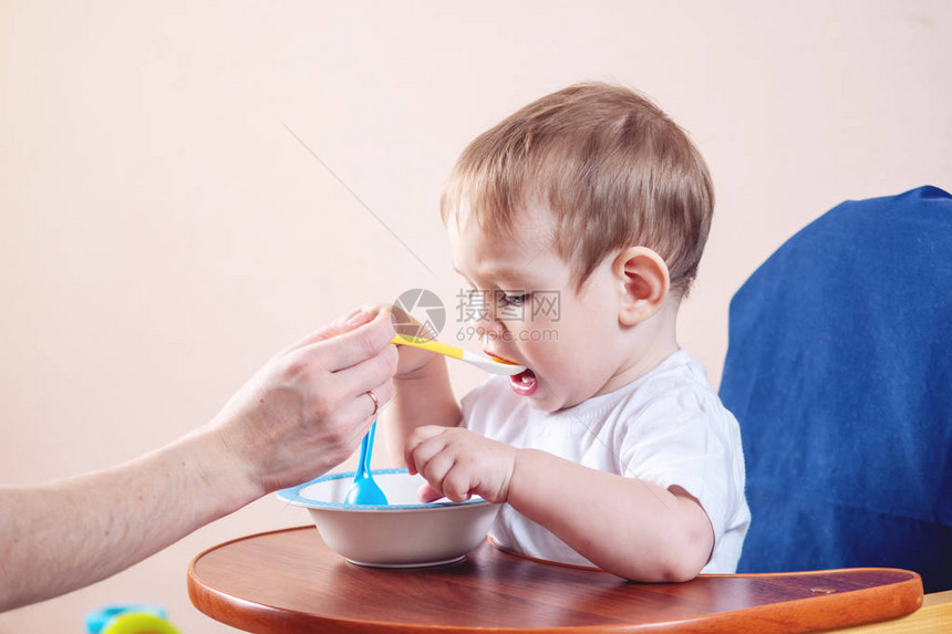 小可爱男孩在厨房的椅子上吃东西妈手握着一勺图片