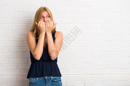金发女人有点紧张害怕在白砖墙背景上亲手张嘴的图片