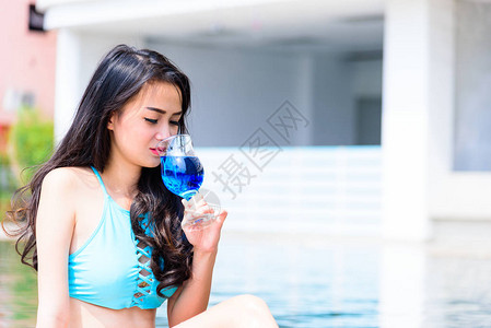 感的亚洲女人在晚上和日落时间喝蓝葡萄酒图片