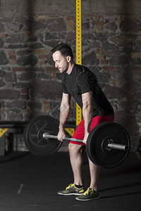 黑色T恤和红色短裤男运动员在有砖墙背景的健身房练习图片