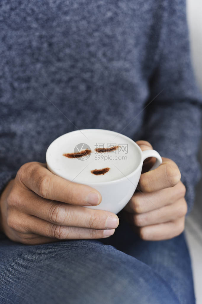 一位坐在沙发或扶椅上手里拿着一杯卡布奇诺咖啡的年轻天主教男子紧闭着图片